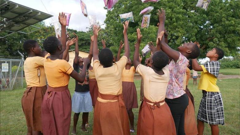 Students in Ghana throw period products in the air